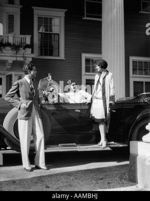 1930ER JAHRE MANN UND ZWEI FRAUEN IN ELEGANTEN KLEIDERN MIT TOURENWAGEN VOR ELEGANTE GROßES HAUS GEPARKT Stockfoto