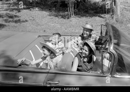 1960ER JAHREN VIERKÖPFIGE FAMILIE IN CABRIO AUF DER SUCHE NACH LINKS Stockfoto