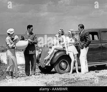 1930ER JAHRE GRUPPE VON FÜNF MÄNNERN & FRAUEN AM 1936 FORD V-8 GEPARKT UFER SPIELEN MIT AUFBLASBAREN STRANDSPIELZEUG Stockfoto