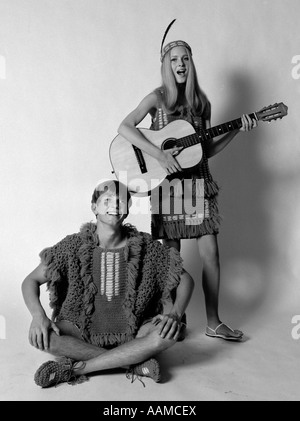 1960S 1970S TEENAGER-PAAR IN GEHÄKELTE KLEIDUNG FRAU MIT FEDER STIRNBAND SPIELEN GITARRE GEKLEIDET MANN SINGEN Stockfoto