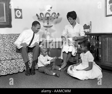 1960ER JAHREN LÄCHELND AFRICAN AMERICAN FAMILIE VATER MUTTER TOCHTER SOHN SITZEN ZUSAMMEN IM WOHNZIMMER Stockfoto