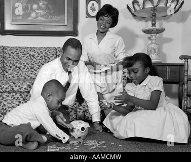 1960ER JAHREN AFROAMERIKANISCHE FAMILIE IM WOHNZIMMER BODEN ZÄHLEN VERÄNDERUNGEN IM SPARSCHWEIN Stockfoto
