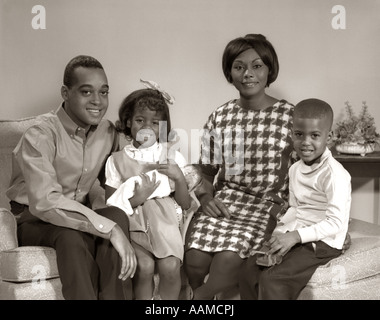 1960ER JAHRE PORTRAIT OF SMILING AFROAMERIKANISCHE FAMILIE SITZT IM WOHNZIMMER TOCHTER HÄLT BABYDOLL Stockfoto