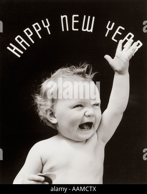 1930ER JAHRE BABY MIT OFFENEM MUND UND HAND HEBEN MIT HAPPY NEW YEAR AUSGESCHRIEBEN IN BOGEN ÜBER KOPF Stockfoto