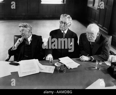 1930S 1940S GRUPPE VON DREI ÄLTEREN GESCHÄFTSLEUTE SITZEN AM KONFERENZTISCH MIT AUFMERKSAMKEIT GERICHTET AUF LAUTSPRECHER NICHT ANGEZEIGT Stockfoto