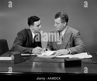 1940S 1950S SITZEN ZWEI MÄNNER SCHREIBTISCH MIT BLICK AUF GESCHÄFTSPAPIEREN Stockfoto