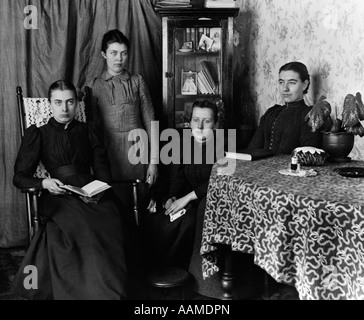 1890S 1895 UMDREHUNG DER JAHRHUNDERT-GRUPPE VON VIER WEIBLICHEN STUDENTEN VERSAMMELTEN SICH UM TISCH MIT BÜCHERN Stockfoto