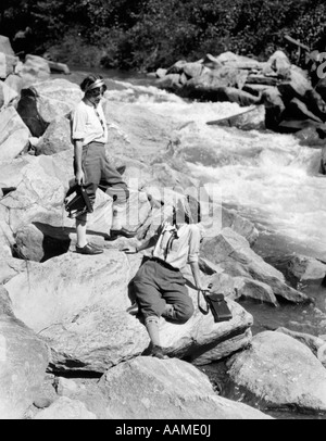 1920ER JAHREN ZWEI FRAUEN SCHWESTERN AUF DEN FELSEN VON CREEK SPRECHEN HOLDING FALTUNG KAMERA Stockfoto