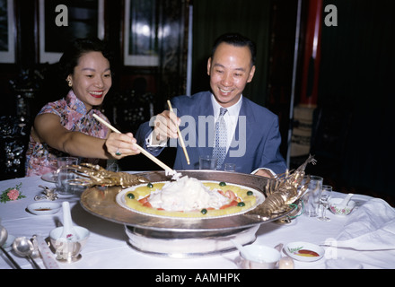 1950ER JAHREN ASIATISCHE PAAR MANN FRAU LÄCHELND ESSEN IN HONG KONG RESTAURANT GROßE ENTREE CHINESISCHES ESSEN STÄBCHEN Stockfoto
