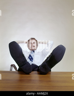 MANN, SITZEND BÜRO SCHREIBTISCH FÜßE HOCH ENTSPANNENDEN SCHNURRBART 1970 1970S RETRO Stockfoto