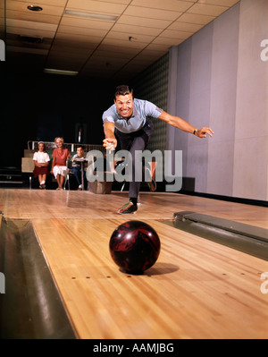 1960ER JAHREN LÄCHELND MANN IN GUTER FORM FREIGABE BOWLINGKUGEL DOWN LANE FRAU 2 SCHAUEN KINDER AUF ERHOLUNG FAMILIE SPAß GASSE Stockfoto