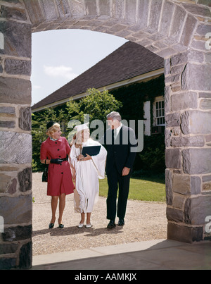 1960ER JAHREN STOLZE ELTERN MIT DIPLOM TOCHTER IN MÜTZE UND MANTEL UNTER TORBOGEN MANN FRAU MÄDCHEN HIGH SCHOOL COLLEGE DREI Stockfoto