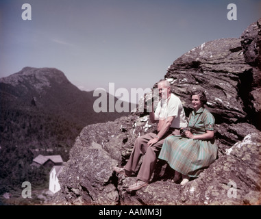 1950ER JAHRE ÄLTERES PAAR AN DER SPITZE DER FELSEN VON MOUNT MANSFIELD VT MANN HAT FERNGLAS FRAU IM GRÜNEN KLEID KAMERA AM HALS IN DEN RUHESTAND REISEN Stockfoto