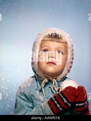 1960ER JAHRE KLEINES MÄDCHEN HÄLT SCHNEE BALL SUCHEN SAD IM HIMMEL ROTE HANDSCHUHE WHITE STRICKEN HUT BLAU JACKE RETRO Stockfoto