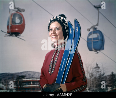 1970 1970S RETRO-FRAU IM WINTER GEAR HUT HOLDING SKI SKILIFT IM HINTERGRUND Stockfoto