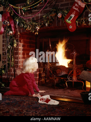 1960ER JAHREN KLEINE BLONDE MÄDCHEN KAMIN DEKORIERT FÜR WEIHNACHTEN HALTEN STRUMPF NOSTALGIE SANTA Stockfoto