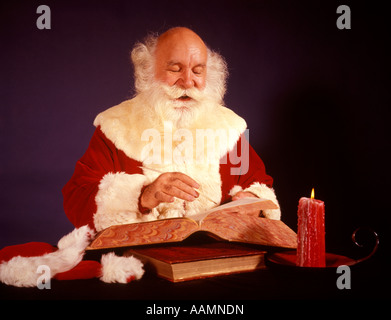 1950ER 1960ER JAHRE 1970ER JAHREN GLATZE WEIHNACHTSMANN SCHREIBEN LISTE IM GROßEN BUCH VON CANDLE LIGHT STUDIO INDOOR Stockfoto