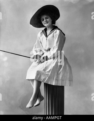 1910S 1920S TRAGEN DAMENKLEID MIT SEEMANN STIL KRAGEN STROH HUT SITZT AUF POST MIT ANGELRUTE Stockfoto