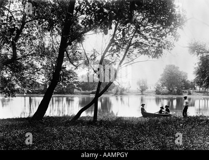 1890S 1900S UMDREHUNG DER JAHRHUNDERT ÄLTER BRUDER BEOBACHTEN GRUPPE DREI JÜNGERER KINDER IM RUDERBOOT AM KLEINEN SEE Stockfoto