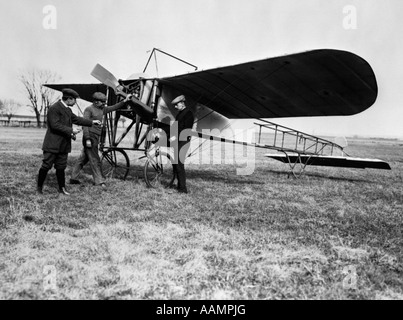 1910ER JAHRE GRUPPE VON DREI MÄNNERN VOR FRÜHEN EINDECKER MIT HAND ON PROPELLER Stockfoto