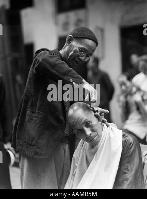 1920ER JAHRE 1930ER JAHRE CHINESISCHER MANN BÜRGERSTEIG BARBIER IN SCHÄDEL RASIEREN EINES ANDEREN MANNES KOPF HONGKONG CHINA Stockfoto