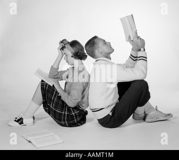 1950ER JAHREN PAAR TEEN JUNGE MÄDCHEN SITZEN RÜCKEN AN RÜCKEN LESEBÜCHER STUDIEREN Stockfoto