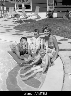 1950ER JAHRE PORTRÄT DER FAMILIE VON VIER SITZEN AM POOL LÄCHELND Stockfoto