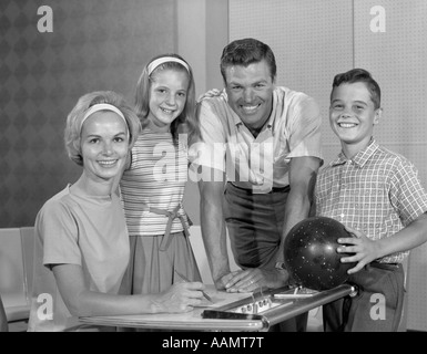 1960ER JAHREN VERSAMMELTEN SICH LÄCHELND 4-KÖPFIGE FAMILIE UM KEGELBAHN SCORING SCHREIBTISCH SOHN MIT BOWLING BALL Stockfoto