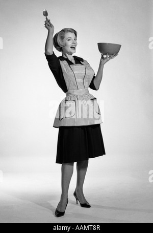 1950ER JAHREN FRAU IN SCHÜRZE HOLDING MISCHENDE SCHÜSSEL UND LÖFFEL ÜBERTRIEBEN AUSDRUCK Stockfoto