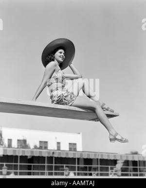 1930ER JAHREN FRAU TRAGEN HUT SITZT IN DER NÄHE VON RAND DES SPRUNGBRETT Stockfoto