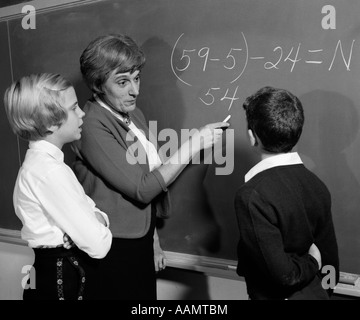 1960ER JAHREN LEHRER AN DER TAFEL MIT MÄNNLICHEN & WEIBLICH SCHÜLER ERKLÄREN MATHEMATISCHE PROBLEM Stockfoto