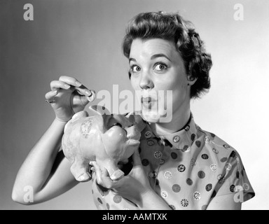 1950ER JAHREN FRAU AUF DER SUCHE AT KAMERA FALLEN GELD IM SPARSCHWEIN Stockfoto