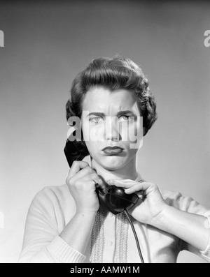 1950ER JAHREN FRAU AN EMPFÄNGER HAND ÜBER RECEIVER BLICK IN DIE KAMERA MIT VERÄRGERT ANGRY AUSDRUCK Stockfoto