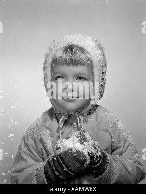 1950ER JAHRE MÄDCHEN POSIERT IN WINTER JACKE HANDSCHUHE UND HALTEN SCHNEE Stockfoto