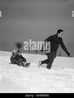 1930ER JAHREN SCHNEE ZIEHEN TOCHTER VATER UND SOHN BERGAB AUF SCHLITTEN IN Stockfoto