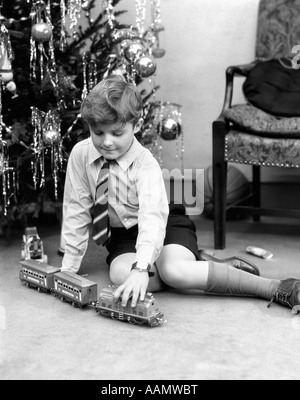 1930ER JAHRE JUNGE SPIELT MIT SPIELZEUGEISENBAHN WEIHNACHTSBAUM Stockfoto