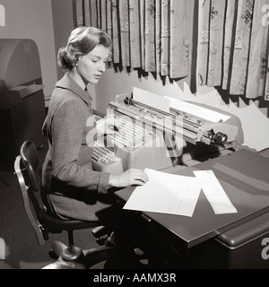 1950ER JAHRE SEKRETÄRIN SITZT AM SCHREIBTISCH LESEN AUS LEDGER MAKING EINTRÄGE ON COMPTOMETER Stockfoto