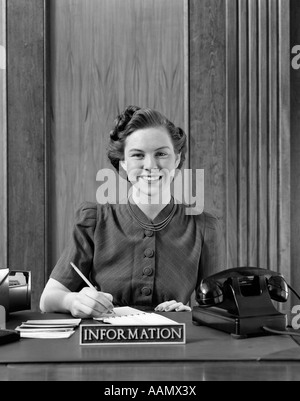 1940ER JAHRE PORTRAIT VON LÄCHELNDEN FRAU INFORMATION DESK EMPFANGSDAME HOLDING BLEISTIFT ÜBER TERMINKALENDER Stockfoto