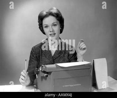 1960ER JAHRE PORTRAIT SEKRETÄRIN SITZT HINTER DER SCHREIBMASCHINE MIT STENO BUCH SEITE & BLEISTIFT IN DER HAND Stockfoto