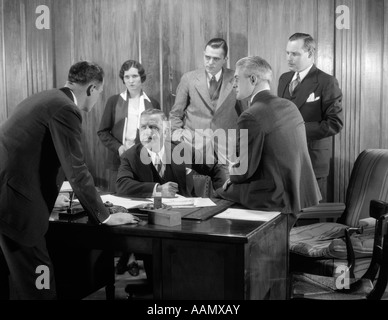 1930ER JAHREN BESORGT BUSINESS GROUP FÜNF MÄNNER UND EINE FRAU IM BÜRO TREFFEN UM DEN CHEF SCHREIBTISCH Stockfoto