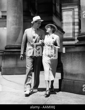 1930ER JAHREN PAAR IN ANZÜGEN UND HÜTEN GEHEN ARM IN ARM Stockfoto