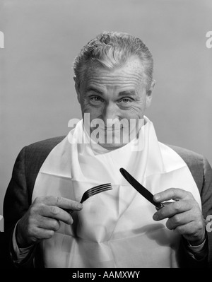 1950S 1960S ÄLTERE MENSCHEN TRAGEN SERVIETTE AS BIB LÄCHELND HOLDING MESSER & GABEL ESSEN DINE VORFREUDE LEBENSMITTEL DIÄT ERNÄHRUNG Stockfoto