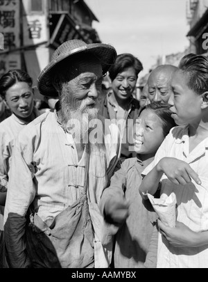 1920S 1930S ÄLTERER ALTE CHINESISCHE MANN MIT BART HUT STROH KULI IM GESPRÄCH MIT JUNGEN MENSCHEN Stockfoto