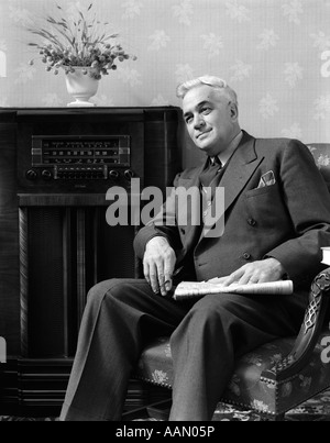 1940ER JAHRE SENIOR MANN SITZT IM WOHNZIMMER HOLDING ZEITUNG RADIO HÖREN Stockfoto