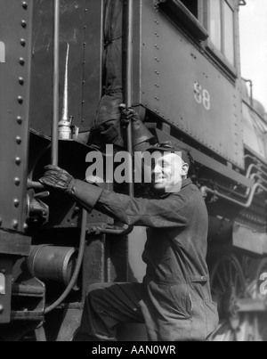 1930ER JAHRE EISENBAHNER IN OVERALLS HUT BRILLE & HANDSCHUHE KLETTERN BIS AUF ZUG Stockfoto