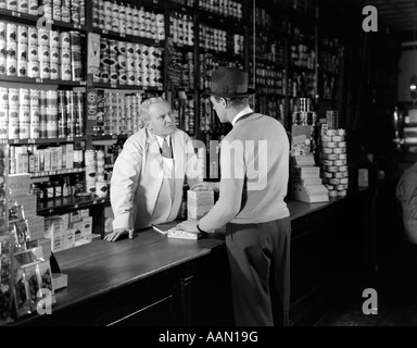 1930S 1940S ZWEI MÄNNER KUNDEN UND ANGESTELLTE IN DER REGEL SPEICHERN IM GESPRÄCH ÜBER ZÄHLER Stockfoto