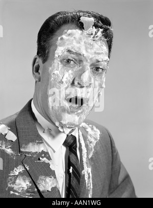 1960ER JAHRE MANN GESICHT SCHULTERN TORTE INS GESICHT MIT BAISER RASIERSCHAUM BEDECKT Stockfoto