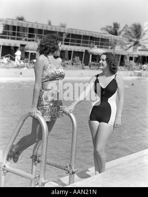 ZWEI FRAUEN IN BADEN ANZÜGE STEHEN NEBEN EINER STÜTZTE SICH AUF POOL LEITER POOL 1930S 1940S Stockfoto