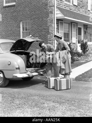 1940ER JAHREN LÄCHELND PAAR FRAU ÜBERGABE MANN GEPÄCK IM KOFFERRAUM DER LIMOUSINE SETZEN IM EINFAHRT VON HOME Stockfoto