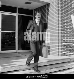 1980ER JAHREN GESCHÄFTSMANN IN NADELSTREIFEN ANZUG ZU FUß AUS GEBÄUDE HINUNTER TREPPE MIT AKTENTASCHE Stockfoto